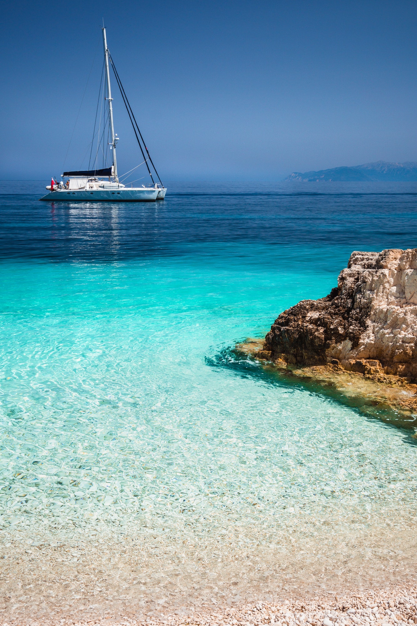 Beautiful calm azure blue lagoon with sailing catamaran yacht boat at anchor. Pure white pebble