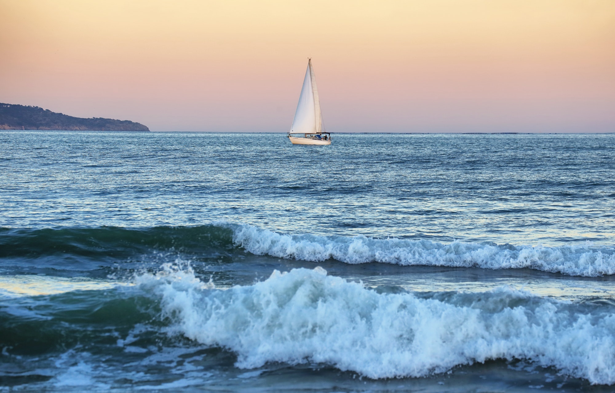 Beautiful azure blue lagoon with sailing catamaran yacht boat at anchor. Pure white pebble beach